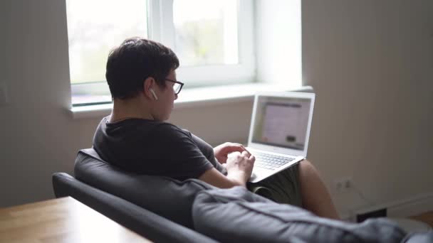 Junger Mann aus dem Kaukasus liest Nachrichten oder arbeitet zu Hause auf dem Sofa. Home Office Konzept. Covid-19-Quarantäne — Stockvideo