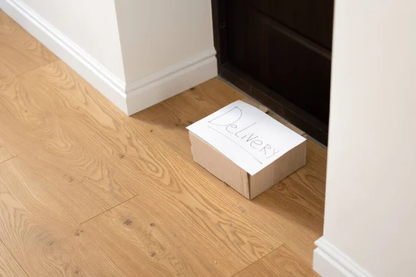 Ung kvinna hemma i handskar och mask tar leverans box från golvet. Kontaktlöst leveranskoncept — Stockfoto