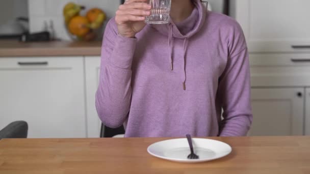 Mujer joven en casa bebe agua y quiere comer. Concepto de ayuno intermitente — Vídeo de stock