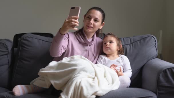 Jovem mãe com a menina criança jogando jogo no telefone em casa. Educação online. Babá com tecnologia — Vídeo de Stock