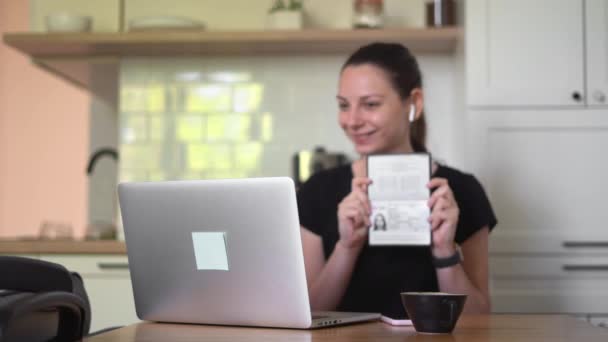 Молодая женщина с паспортом и ноутбуком делает электронную проверку по видеосвязи. Открытие банковского счета — стоковое видео