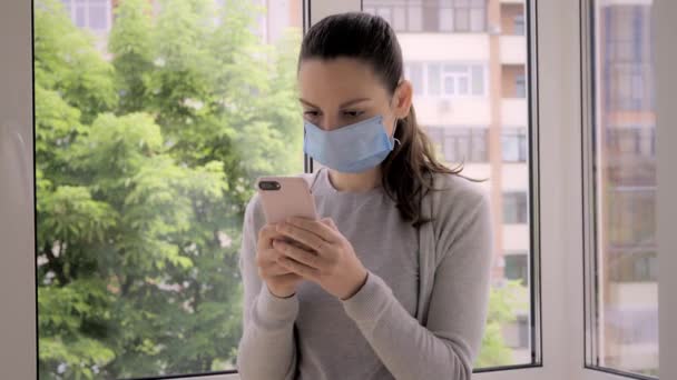 Jeune femme avec masque facial et téléphone à l'extérieur. Vérification des nouvelles, application de suivi des contacts, alerte covid-19 — Video