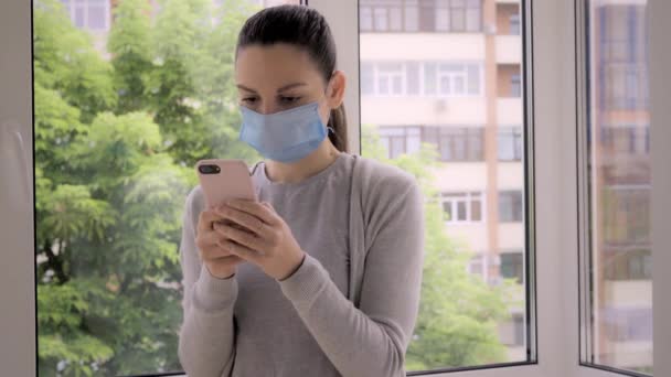 Молодая женщина в маске и телефоне на улице. Проверка новостей, приложение для отслеживания контактов, тревога covid-19 — стоковое видео