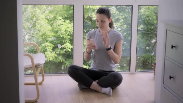 Молодая женщина с телефоном медитирует с онлайн тренером или влиятельным человеком. Приложение для медитации. Covid-19 Locdown — стоковое видео