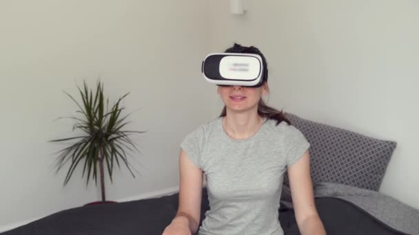 Young woman sitting in bedroom with VR glasses and using AR for entertainment, education, learning, shopping — Stock Video