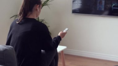 Oturma odasında elinde uzaktan kumandayla oturan ve VOD 'nin online yayın platformunu izleyen bir kadın.