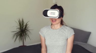 Genç bir kadın yatak odasında VR gözlükleriyle oturuyor ve AR 'ı eğlence, eğitim, öğrenme ve alışveriş için kullanıyor.