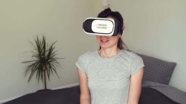 Jonge vrouw zit in de slaapkamer met VR bril en het gebruik van AR voor entertainment, onderwijs, leren, winkelen — Stockvideo