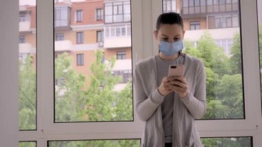 Yüzü maskeli ve dışarıda telefonu olan genç bir kadın. Haberleri kontrol ediyorum, iletişim takip uygulaması, covid-19 alarmı.