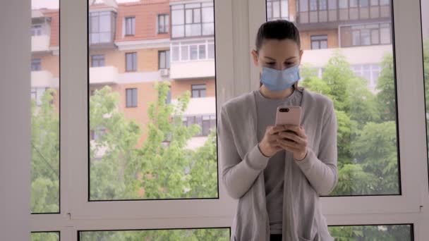 Młoda kobieta z maską na twarzy i telefonem na zewnątrz. Sprawdzanie wiadomości, aplikacja śledząca kontakt, alarm covid-19 — Wideo stockowe