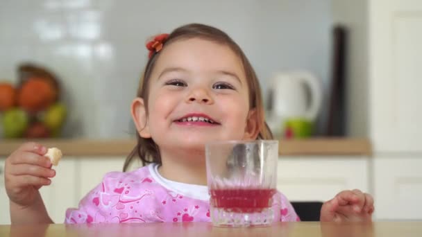 Csinos kisgyerek eszik nasit és iszik egy pohár gyümölcslevet. Vicces arckifejezés. — Stock videók