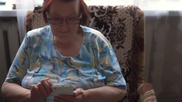 Ηλικιωμένη γυναίκα 80 ετών χρησιμοποιεί smartphone στο σπίτι. Online αγορές, blog συνταγή, βιντεοκλήση. Τεχνικός σάβιος — Αρχείο Βίντεο