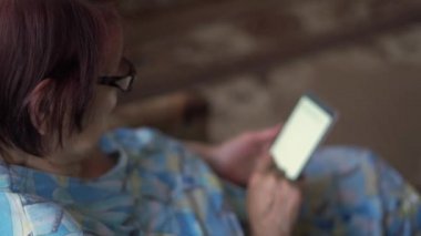 Yaşlı kadın 80 'li yaşlarda, evde akıllı telefon kullanıyor. İnternetten alışveriş, yemek tarifi blogu, video görüşmesi. Teknoloji saavy