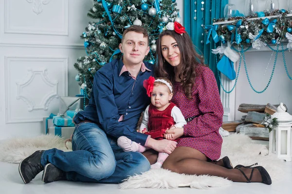Hermosa chica con mamá y papá sentados cerca del árbol de Navidad en casa. Una familia feliz. Feliz Navidad y un feliz año nuevo . Imagen De Stock
