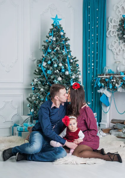 Hermosa chica con mamá y papá sentados cerca del árbol de Navidad en casa. Una familia feliz. Feliz Navidad y un feliz año nuevo . Imagen de archivo
