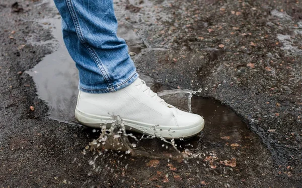 White boots in a muddy puddle on an asphalt road. Close-up. Spray from the boots.