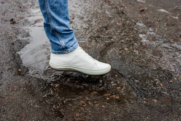 Hvite støvler i en sølepytt på en asfaltvei. Nære på. Spray av støvlene . – stockfoto