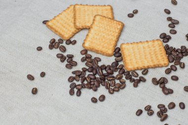 Arka plan gri kumaş eski yapılmış ve kaba çuval bezi, hangi belirli bir miktarda kahverengi kahve çekirdekleri sarı dikdörtgen bisküvi ile yatıyor