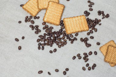 Arka plan gri kumaş eski yapılmış ve kaba çuval bezi, hangi belirli bir miktarda kahverengi kahve çekirdekleri sarı dikdörtgen bisküvi ile yatıyor