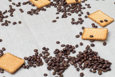 Arka plan gri kumaş eski yapılmış ve kaba çuval bezi, hangi belirli bir miktarda kahverengi kahve çekirdekleri sarı dikdörtgen bisküvi ile yatıyor