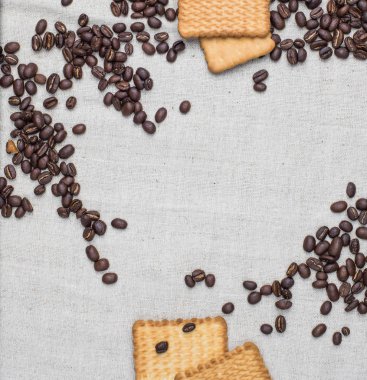 Arka plan gri kumaş eski yapılmış ve kaba çuval bezi, hangi belirli bir miktarda kahverengi kahve çekirdekleri sarı dikdörtgen bisküvi ile yatıyor