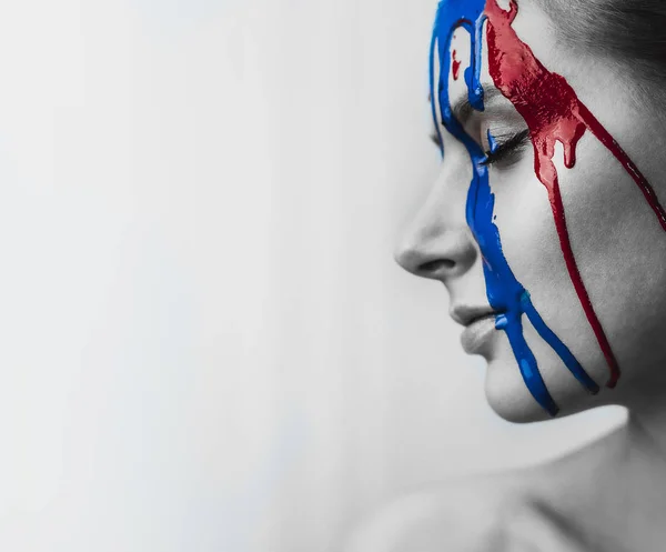 Boya kadın yüzüne yakın çekim. Yüzünde kırmızı ve mavi boya akar. Sanatsal boya sert bir yüz portresi. Siyah ve beyaz fotoğraf yüz boya.