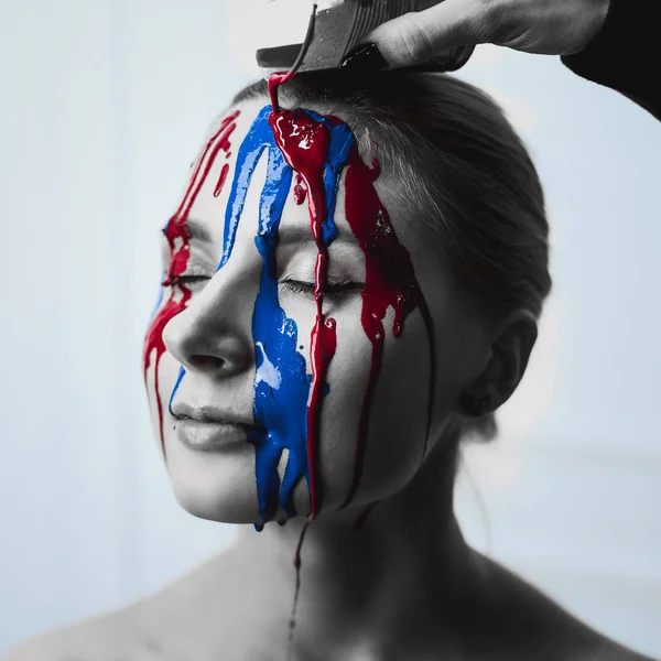 Peins sur le visage féminin, gros plan. Flux de peinture rouge et bleue sur le visage. Portrait artistique d'un visage dur en peinture. Photos noir et blanc visage dans la peinture . — Photo