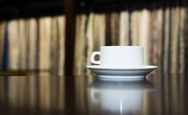 White ceramic cup and saucer on a dark wooden background. Place for your text. Reflection of the cup on the table