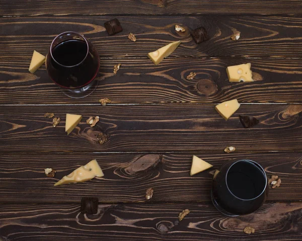 Due bicchieri di vino, formaggio, noce greca, caramelle al cioccolato su sfondo di legno, vista dall'alto — Foto Stock