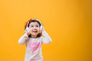 Yumuşak kulaklık, çocuksu duygular sarı bir arka plan üzerinde küçük neşeli mutlu güzel kız ayakta izole.