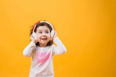 Yumuşak kulaklık, çocuksu duygular sarı bir arka plan üzerinde küçük neşeli mutlu güzel kız ayakta izole.