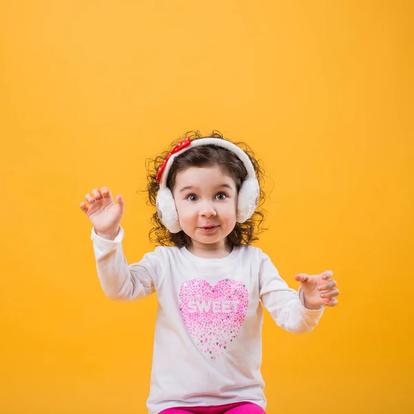 Yumuşak kulaklık, çocuksu duygular sarı bir arka plan üzerinde küçük neşeli mutlu güzel kız ayakta izole.