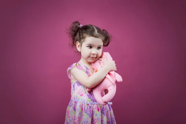 Elegante niña en un vestido rojo abraza suavemente a un conejo de peluche . —  Fotos de Stock