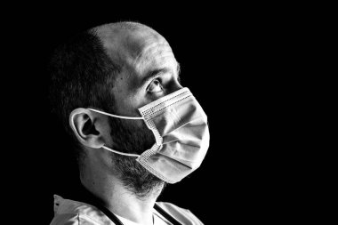 Maske takan bir erkek doktorun yakın portresi ve steteskop mesafeye bakıyor.