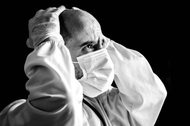Maske takmış, steteskop takmış ve elleri başında endişeli bir erkek doktorun portresi.