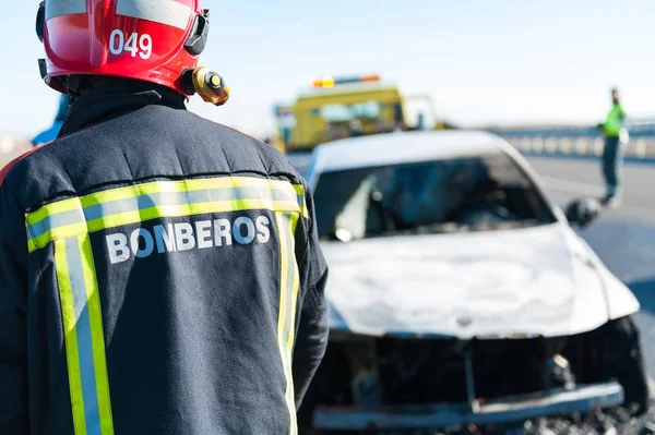 Bombeiros que trabalham ao pé da estrada no incêndio de um veículo — Fotografia de Stock