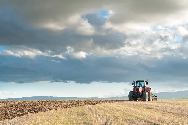 Traktor területén az előtérben napnyugtakor ég — Stock Fotó