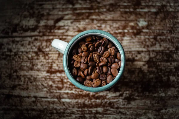 Granos de café sin moler en taza y en mesa de madera — Foto de Stock