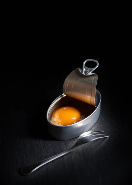Lata de aluminio con yema de huevo en el interior aislada sobre fondo negro — Foto de Stock