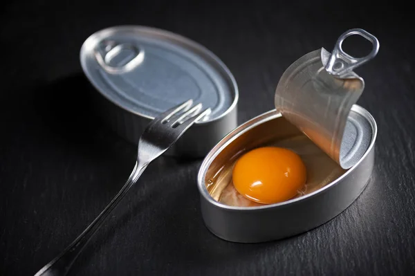 Lata de aluminio con yema de huevo en el interior aislada sobre fondo negro — Foto de Stock