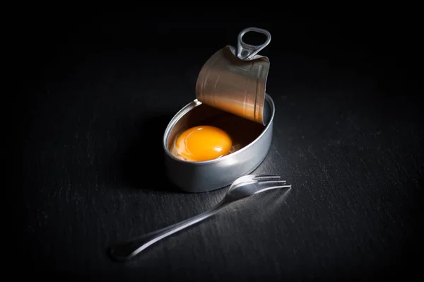 Lata de aluminio con yema de huevo en el interior aislada sobre fondo negro — Foto de Stock