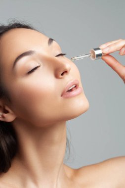 Mükemmel cilde sahip genç ve güzel bir kadın pipette yaşlanmaya duyarlı serum kullanıyor. Cilt bakımı ve yaş kozmetiği