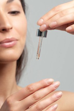 Mükemmel cilde sahip genç ve güzel bir kadın pipette yaşlanmaya duyarlı serum kullanıyor. Cilt bakımı ve yaş kozmetiği