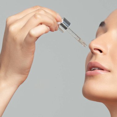 Mükemmel cilde sahip genç ve güzel bir kadın pipette yaşlanmaya duyarlı serum kullanıyor. Cilt bakımı ve yaş kozmetiği