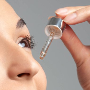 Mükemmel cilde sahip genç ve güzel bir kadın pipette yaşlanmaya duyarlı serum kullanıyor. Cilt bakımı ve yaş kozmetiği