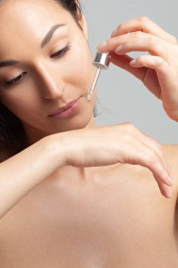 Mükemmel cilde sahip genç ve güzel bir kadın pipette yaşlanmaya duyarlı serum kullanıyor. Cilt bakımı ve yaş kozmetiği