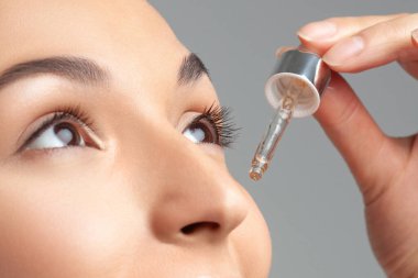 Mükemmel cilde sahip genç ve güzel bir kadın pipette yaşlanmaya duyarlı serum kullanıyor. Cilt bakımı ve yaş kozmetiği