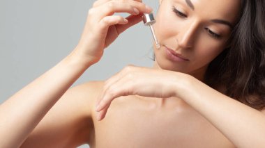 Mükemmel cilde sahip genç ve güzel bir kadın pipette yaşlanmaya duyarlı serum kullanıyor. Cilt bakımı ve yaş kozmetiği