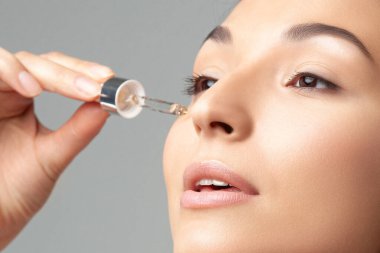 Mükemmel cilde sahip genç ve güzel bir kadın pipette yaşlanmaya duyarlı serum kullanıyor. Cilt bakımı ve yaş kozmetiği