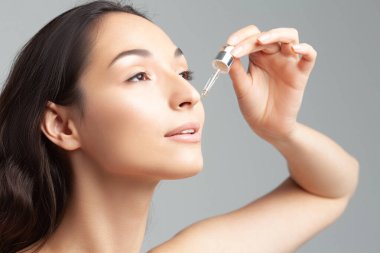 Mükemmel cilde sahip genç ve güzel bir kadın pipette yaşlanmaya duyarlı serum kullanıyor. Cilt bakımı ve yaş kozmetiği
